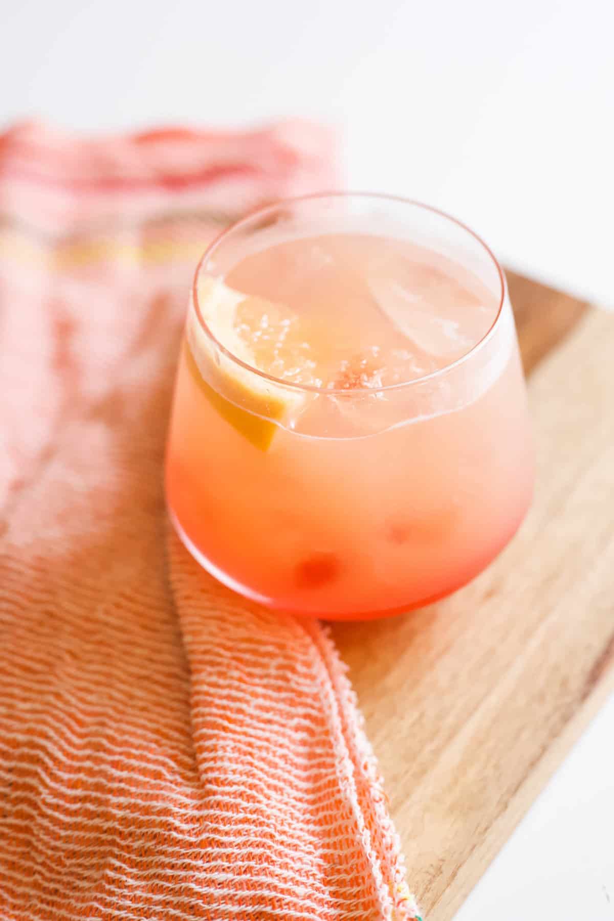 Grapefruit Sunrise cocktail in a short cocktail glass on a wood tray next to an orange fabric napkin.