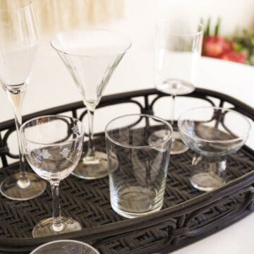 A square image of different types of cocktail glassware on a black tray on a table.