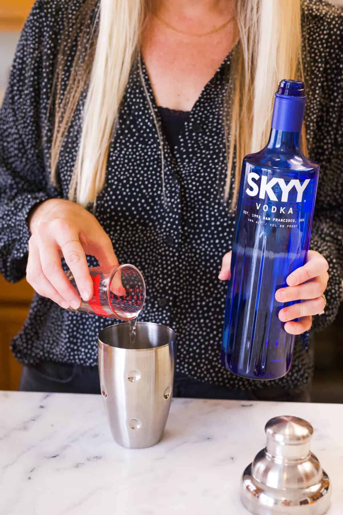 Woman adding vodka to a cocktail shaker at a counter.