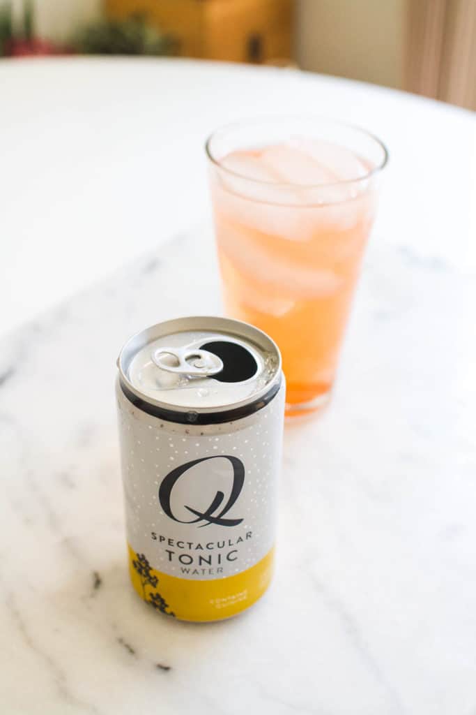 A can of tonic on a table next to a glass holding Aperol and gin.
