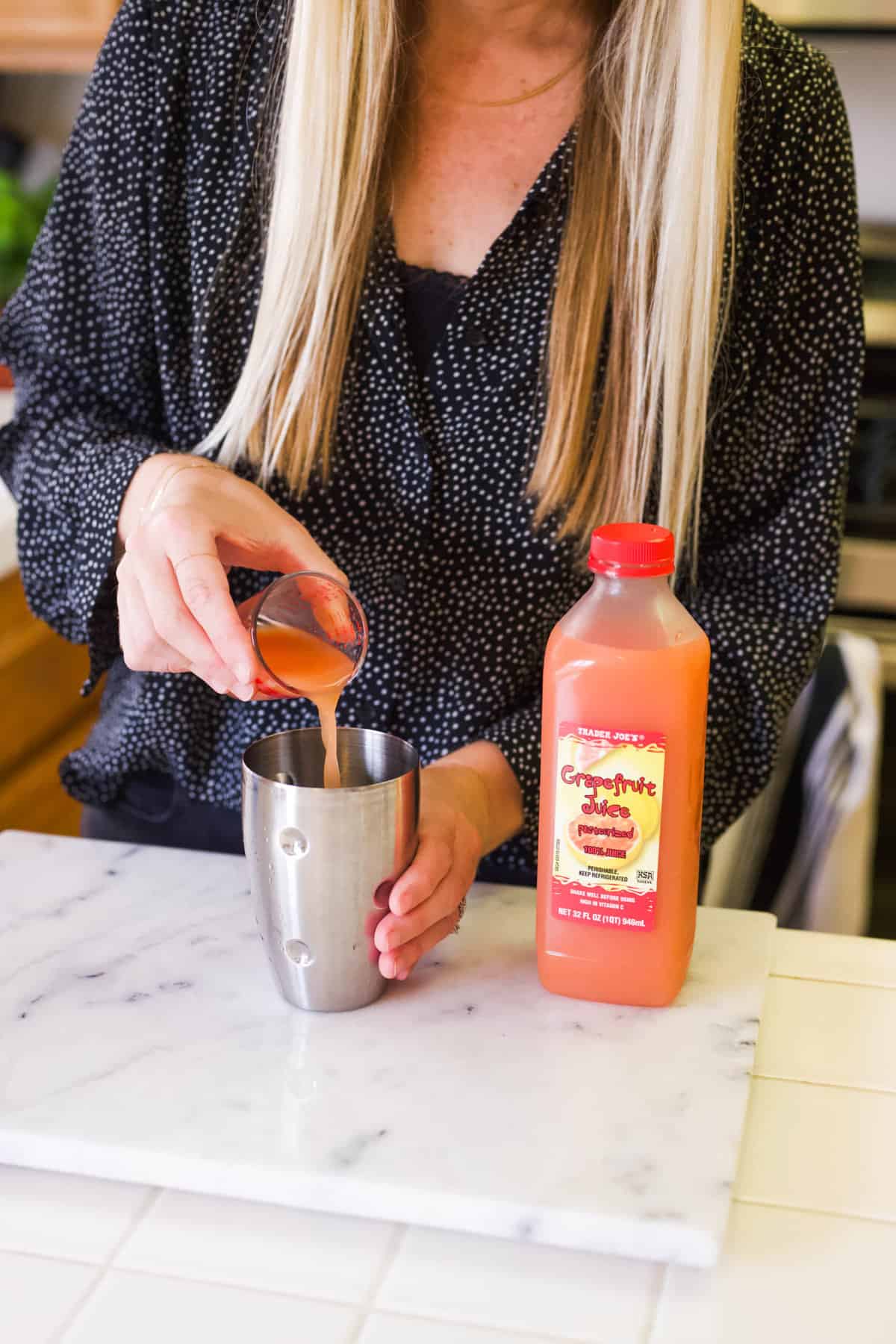 Woman adding grapefruit juice to a cocktail shaker from a jigger.