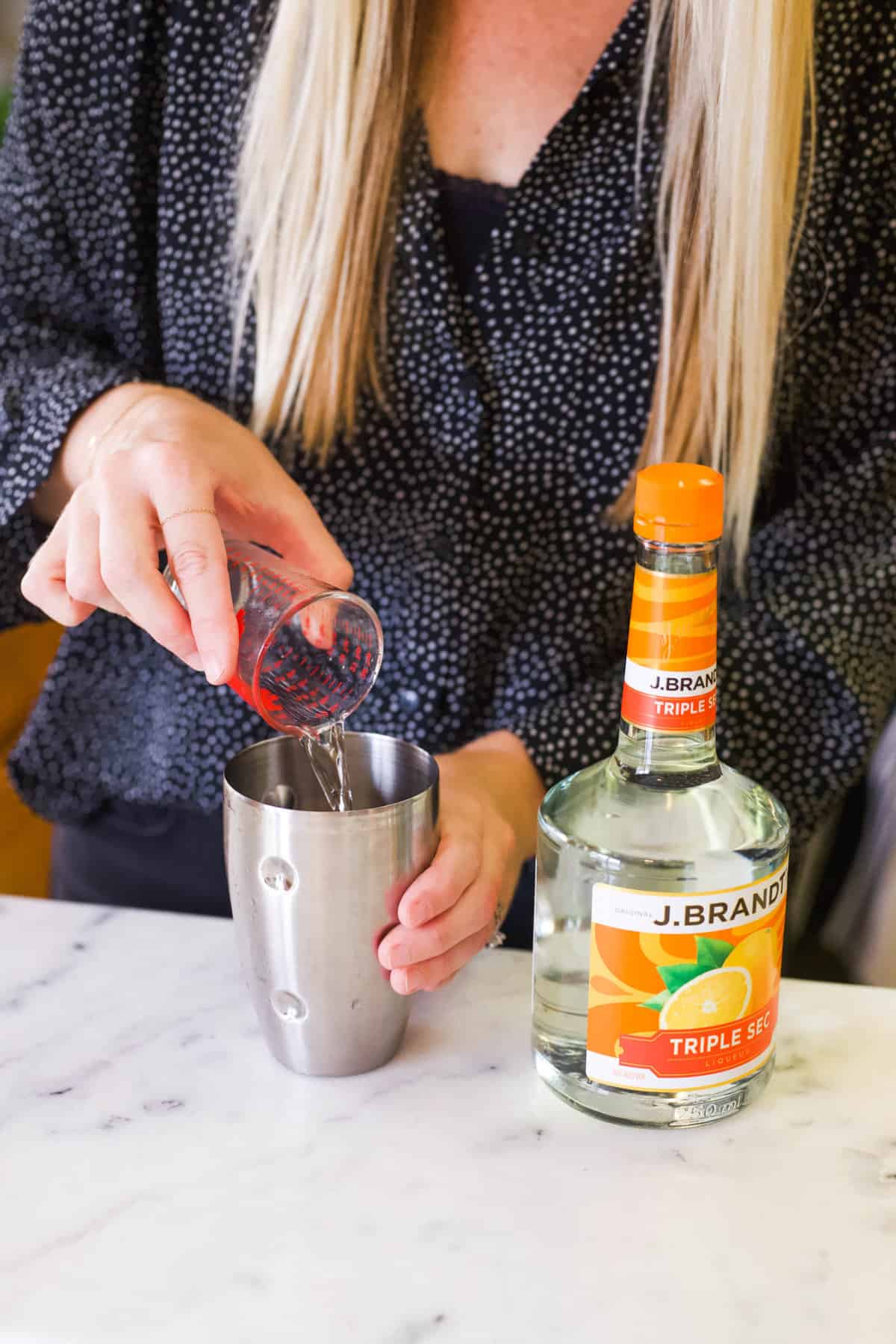 Woman adding Triple Sec to a cocktail shaker from a jigger.