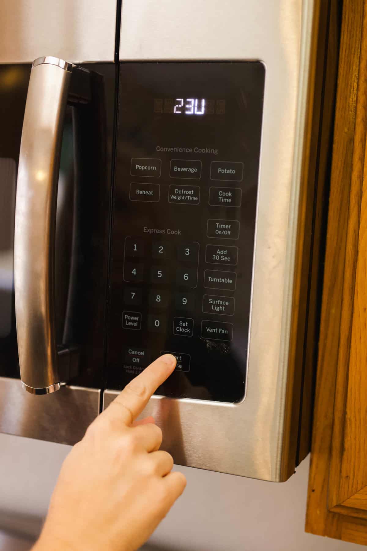 Hand pushing buttons on a microwave.