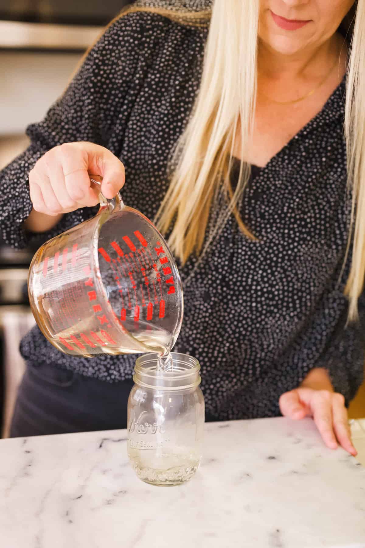 Woman pouring microwave simple syrup from a large glass measuring cup into a mason jar.
