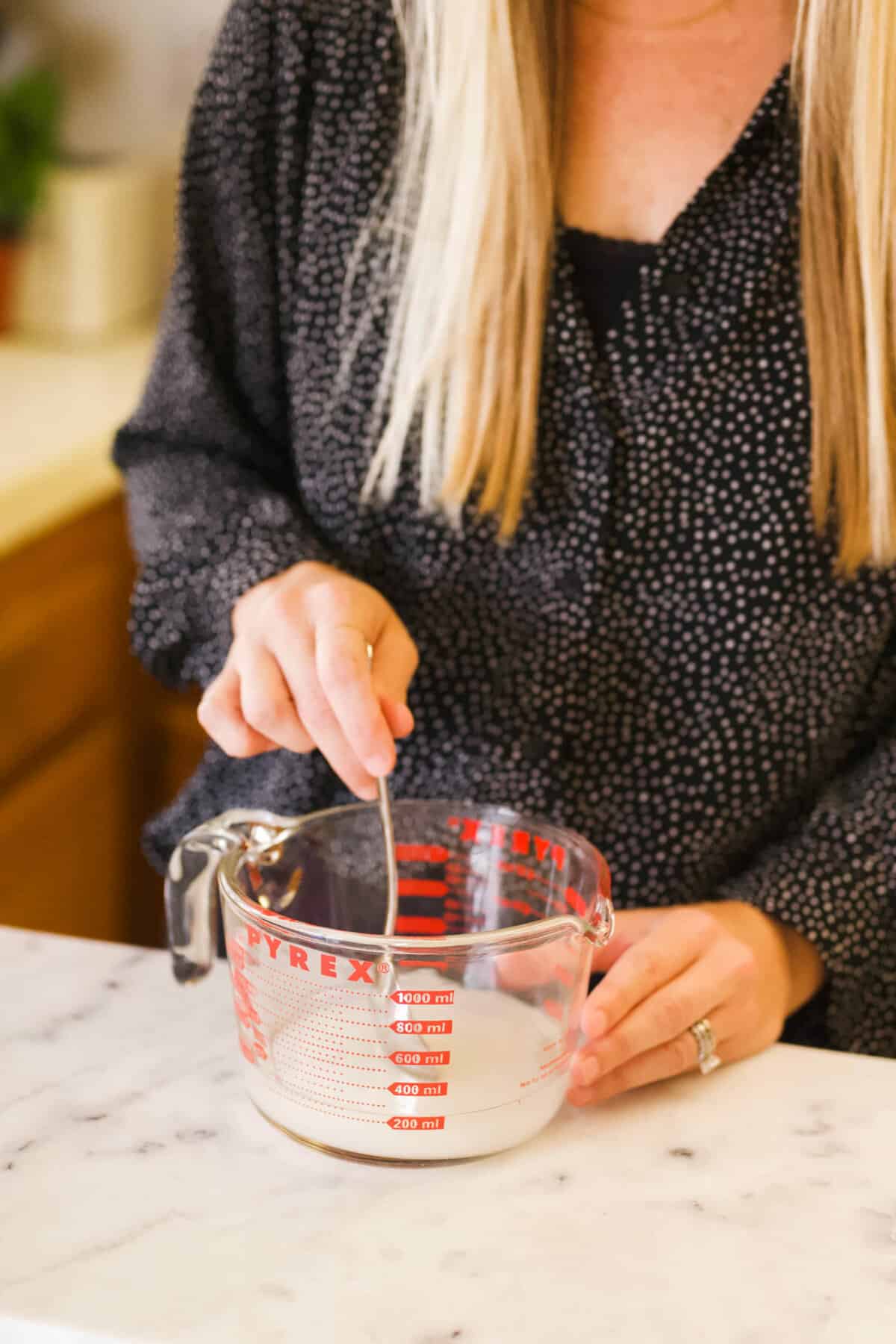 Woman stirring sugar and water in a glass measuring cup to make simple syrup.