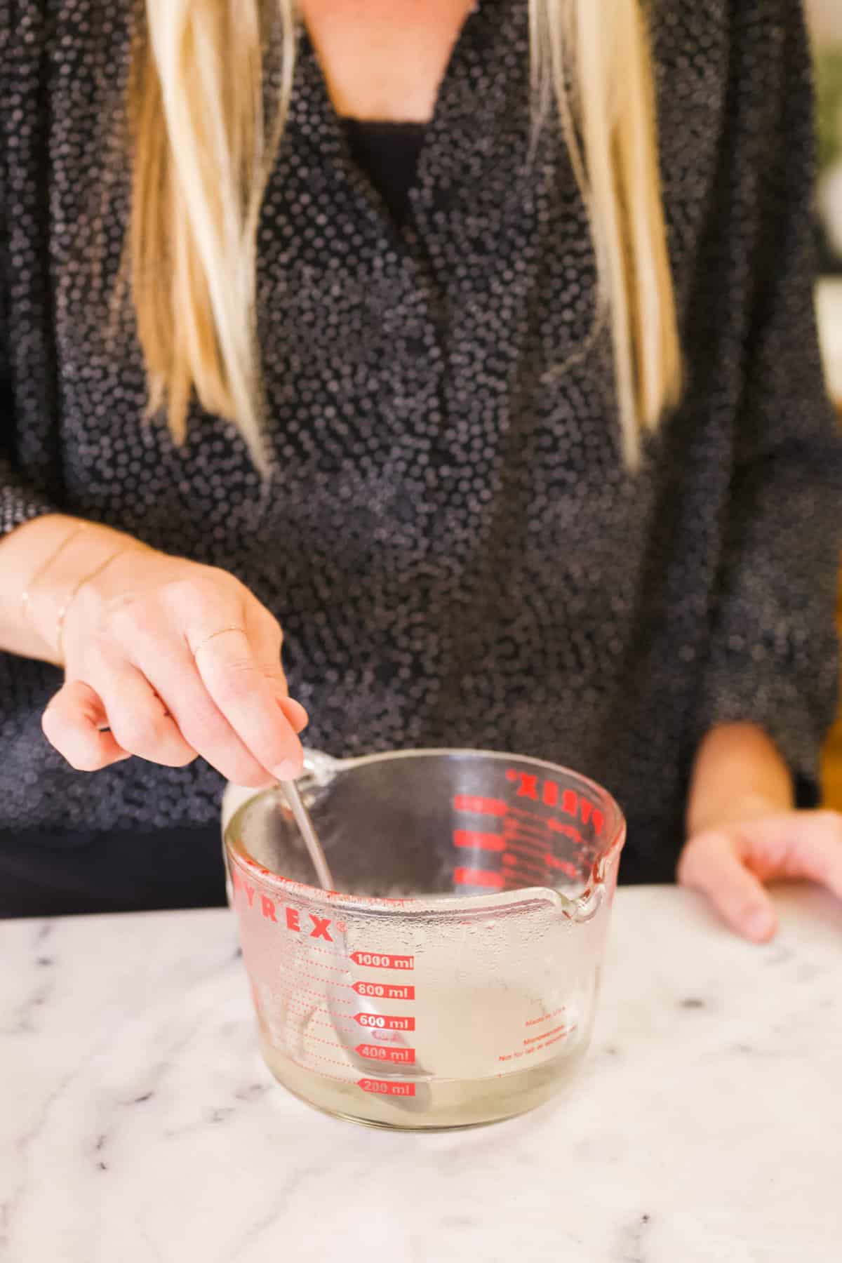 Woman stirring simple syrup in a glass measuring cup.