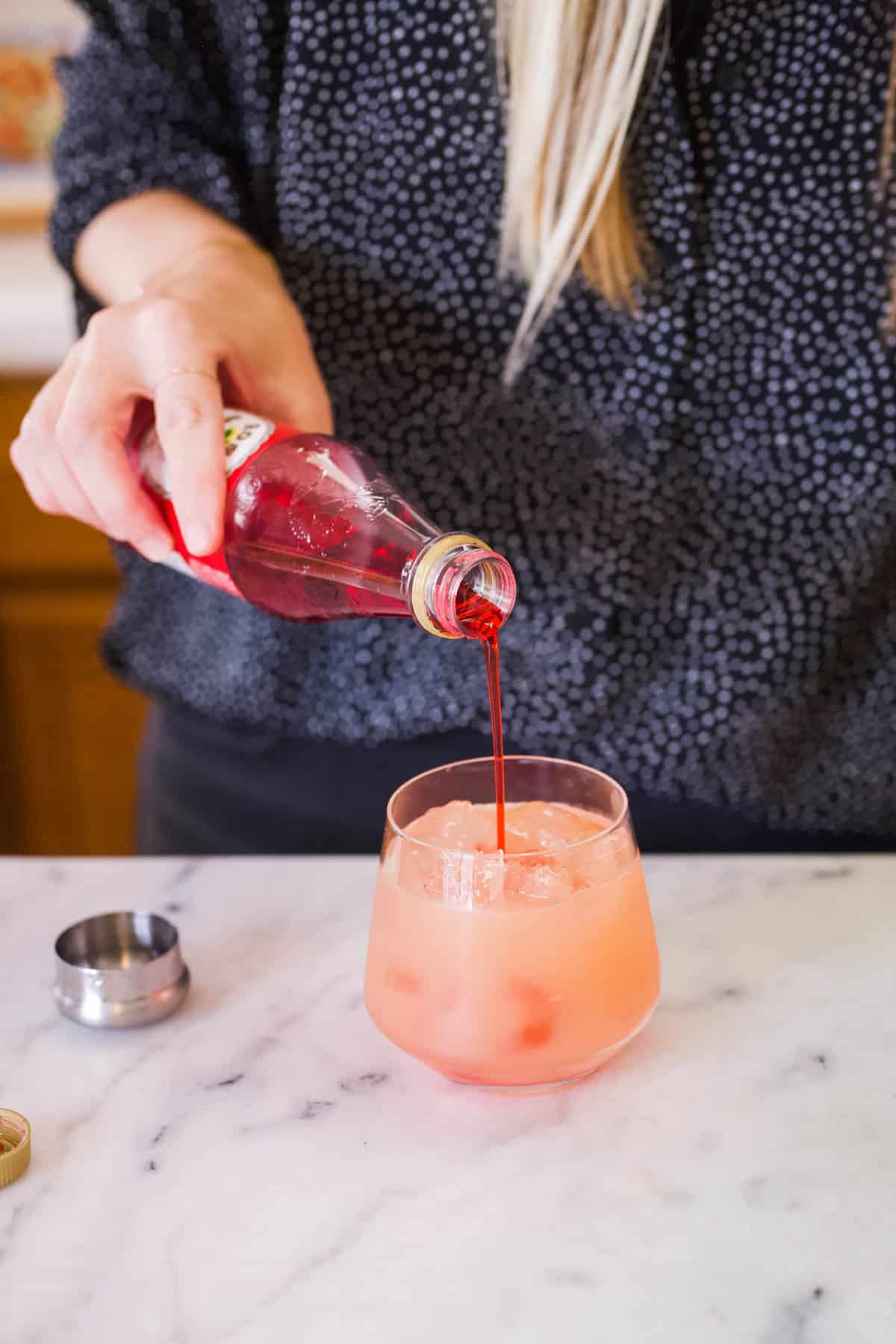 Woman adding grenadine to a short cocktail glass for a sunrise cocktail recipe.