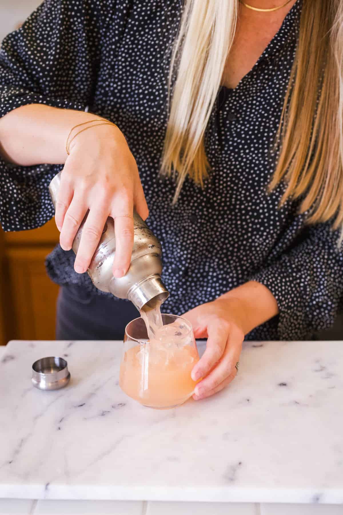 Woman straining a cocktail from a shaker into a cocktail glass.