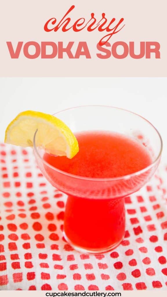 Text: Cherry Vodka Sour with a bright pink drink in a stemless cocktail glass on a table.