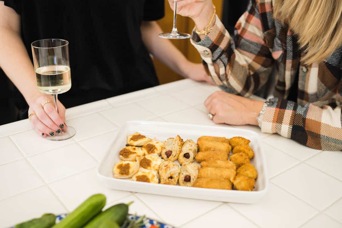 Women with wine glasses at a counter next to a tray of warm appetizers.