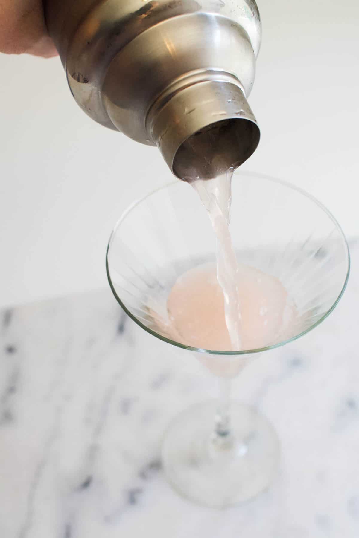 A pink cocktail being strained from a cocktail shaker into a martini glass.