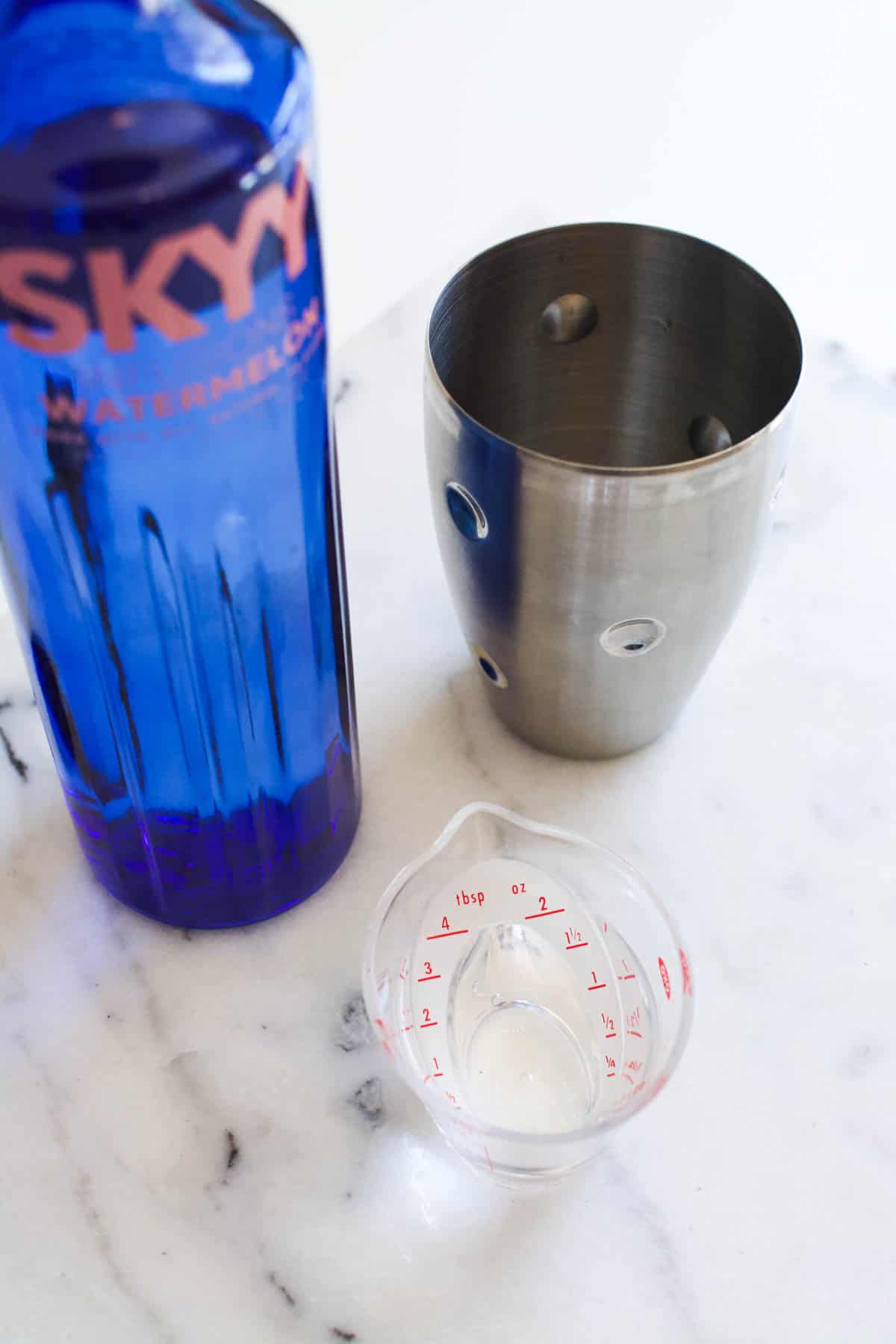 A small measuring jigger with vodka next to a cocktail shaker.