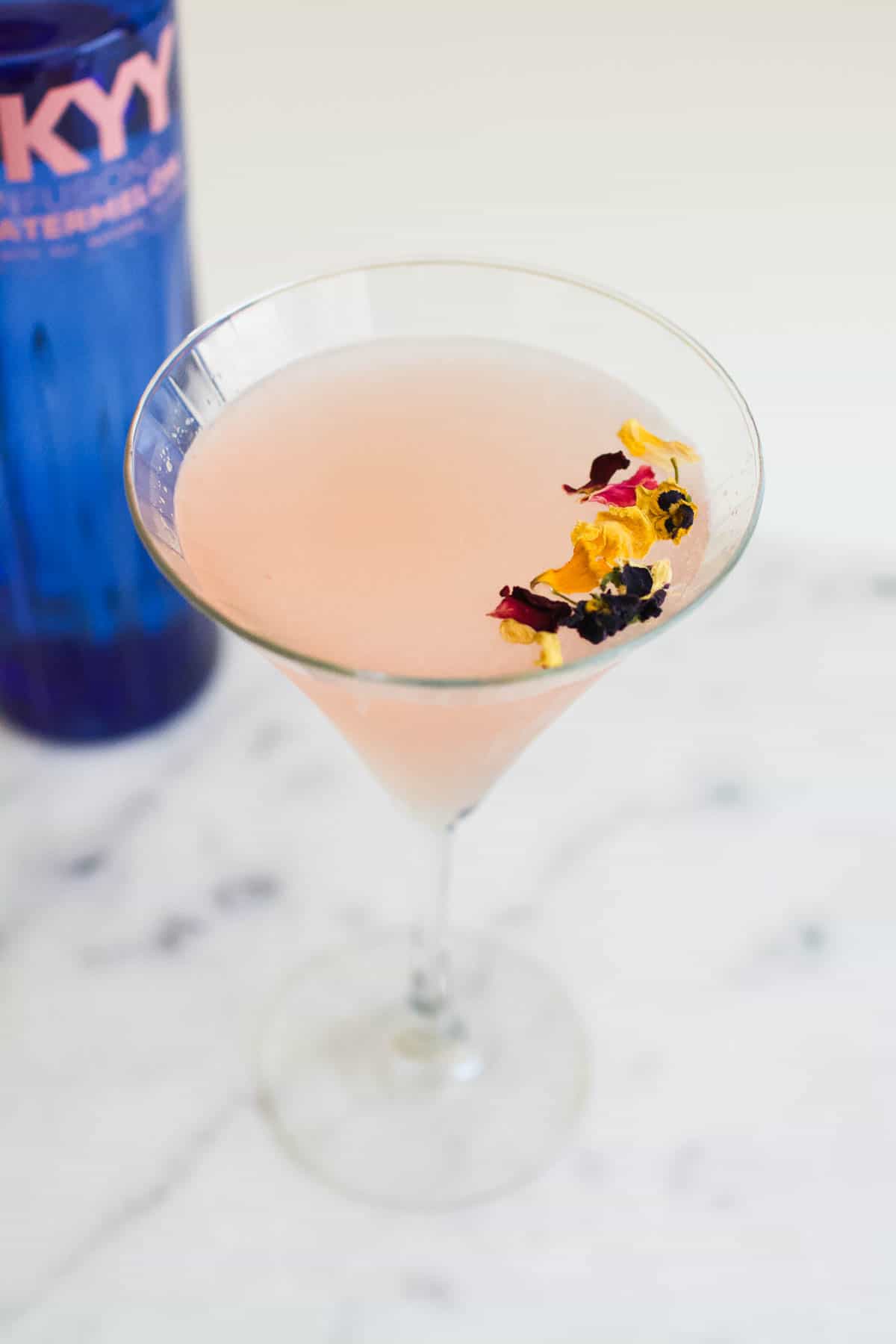 Edible flowers garnishing a pink watermelon gimlet in a martini glass.
