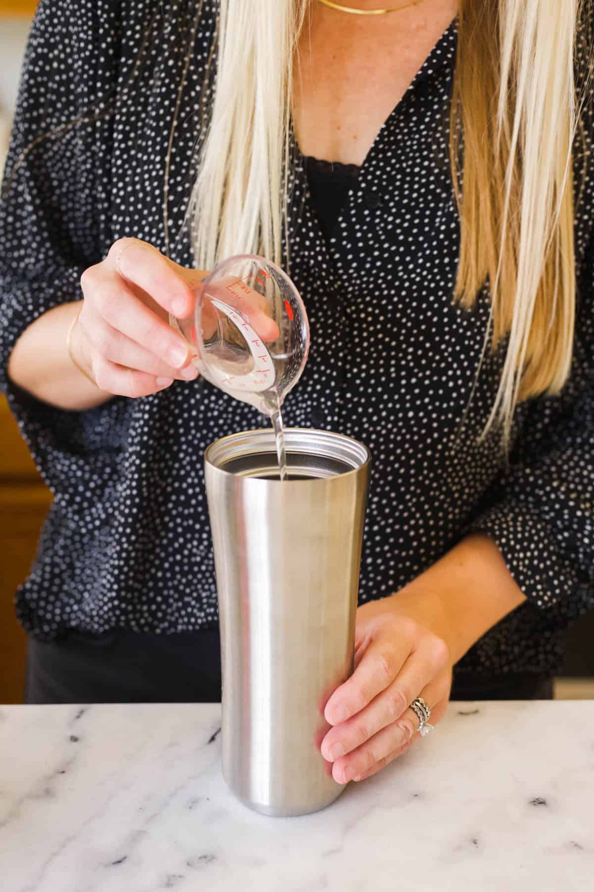 A woman adding simple syrup to a cocktail shaker.