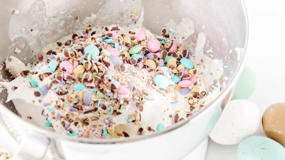 The bowl of a mixer with cream cheese and crushed M&Ms candies for an Easter dessert dip.