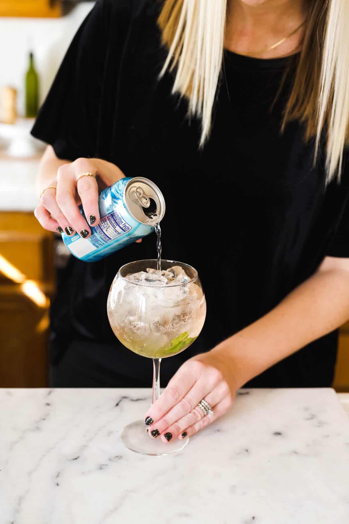 Woman pouring a can of soda water into a spritz cocktail.