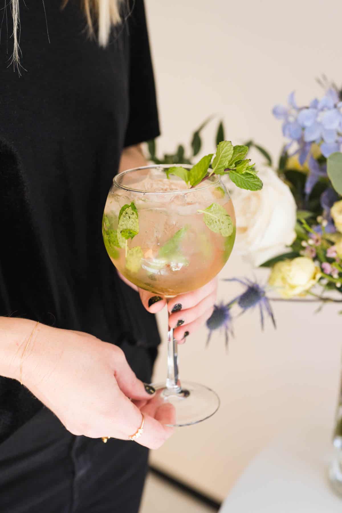 Woman holding a Hugo Spritz garnished with fresh mint.