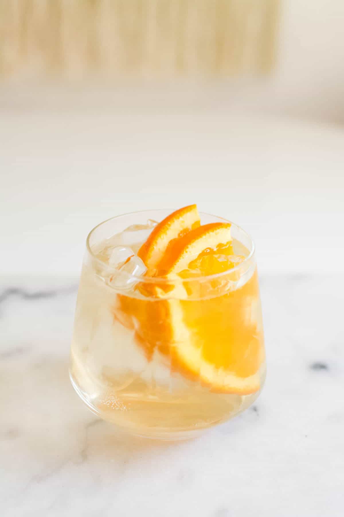 Glass of St Germain and Soda garnished with fresh orange slices on a marble countertop.