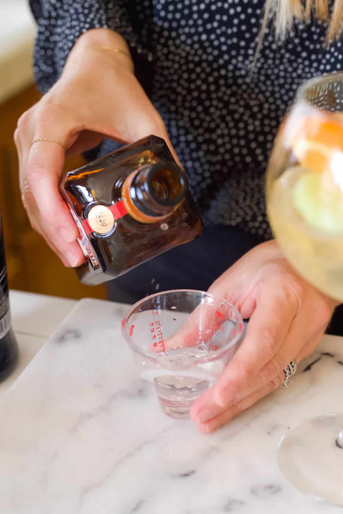 Woman adding Cointreau to a measuring cup.