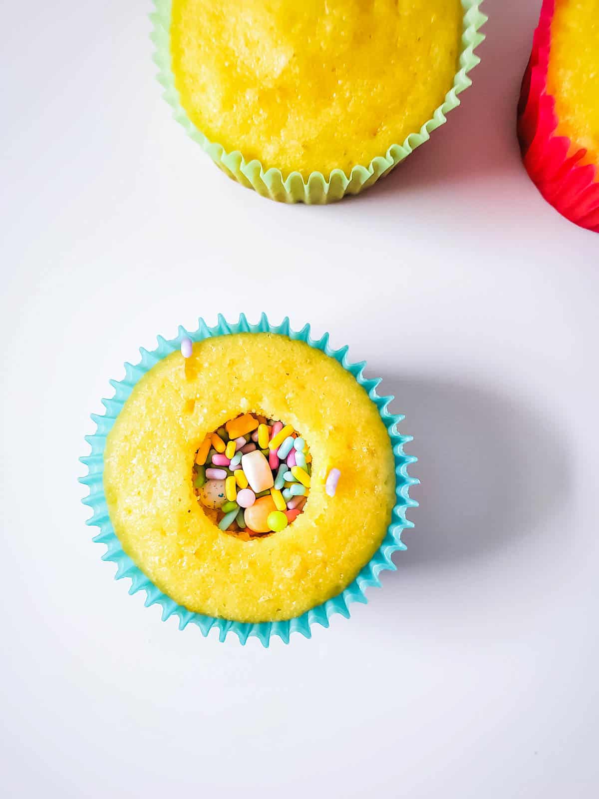 Baked cupcakes on a table with one filled with Easter Sprinkles.