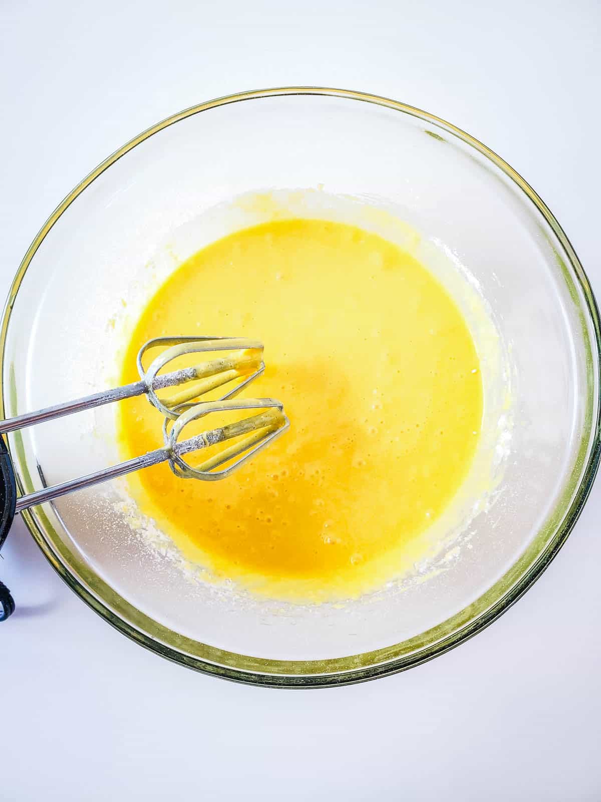 A glass bowl on a counter with boxed cake mix batter and hand held mixer whisks.