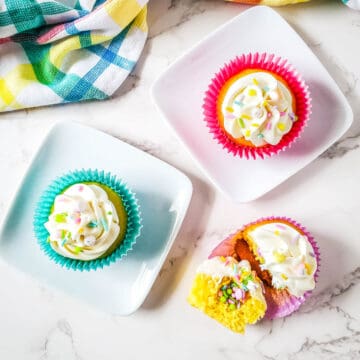 3 Easter cupcakes on a table with one cut open to show a surprise inside with Easter sprinkes.