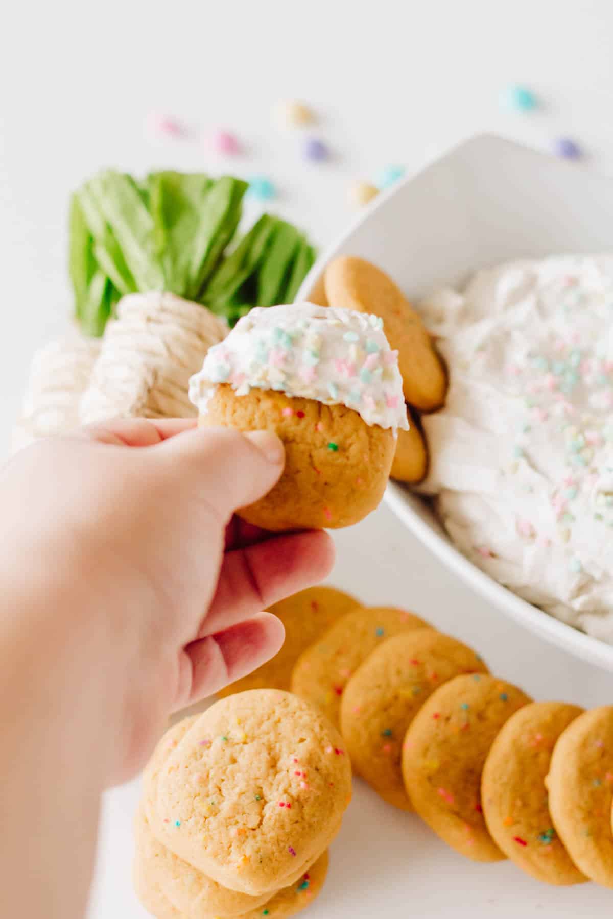 A kid holding a cookie dipped in a cream cheese cake mix dip.