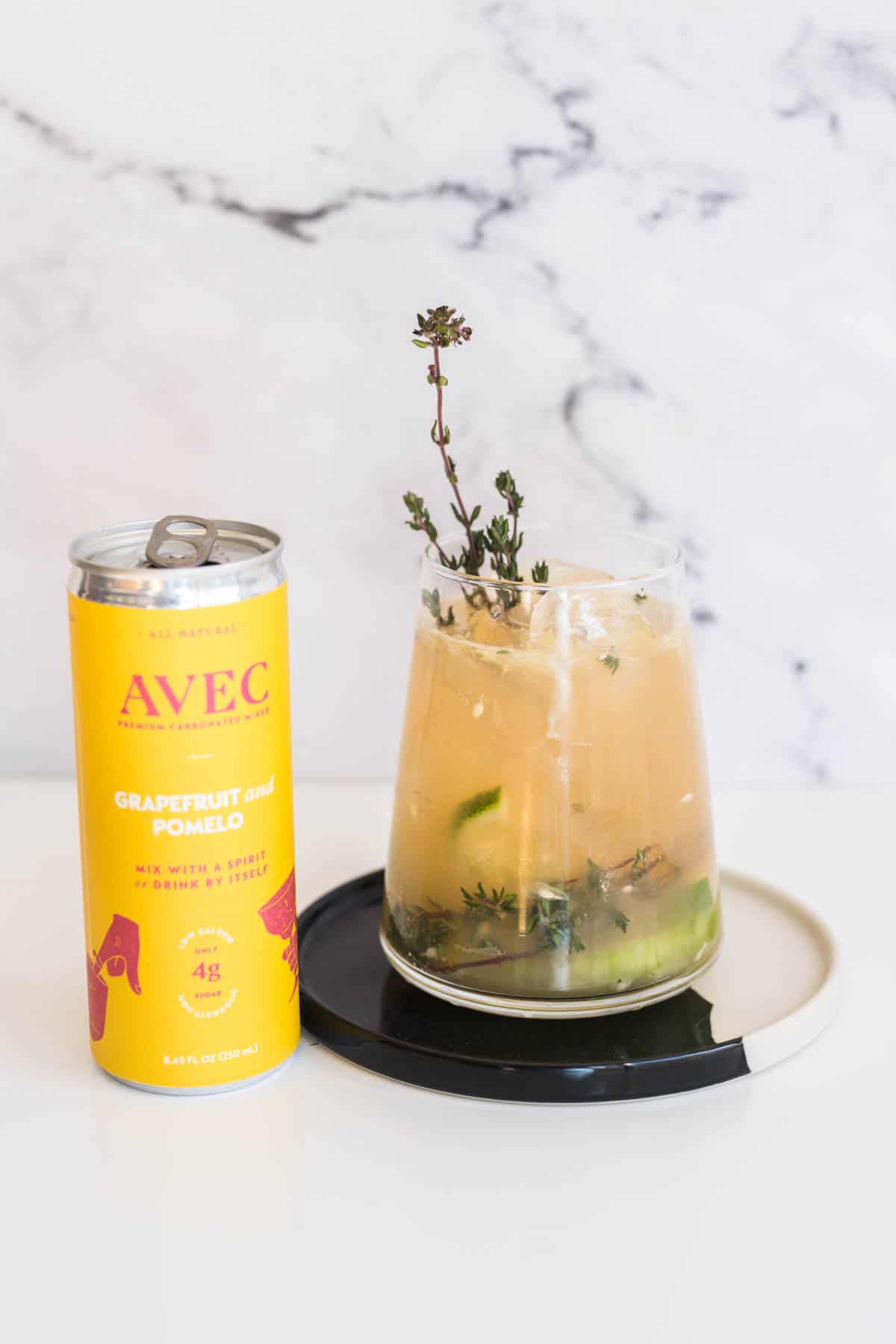 Grapefruit mocktail garnished with fresh thyme next to a can of Avec.