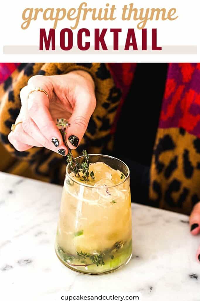 Woman garnishing a grapefruit mocktail with a sprig of fresh thyme.