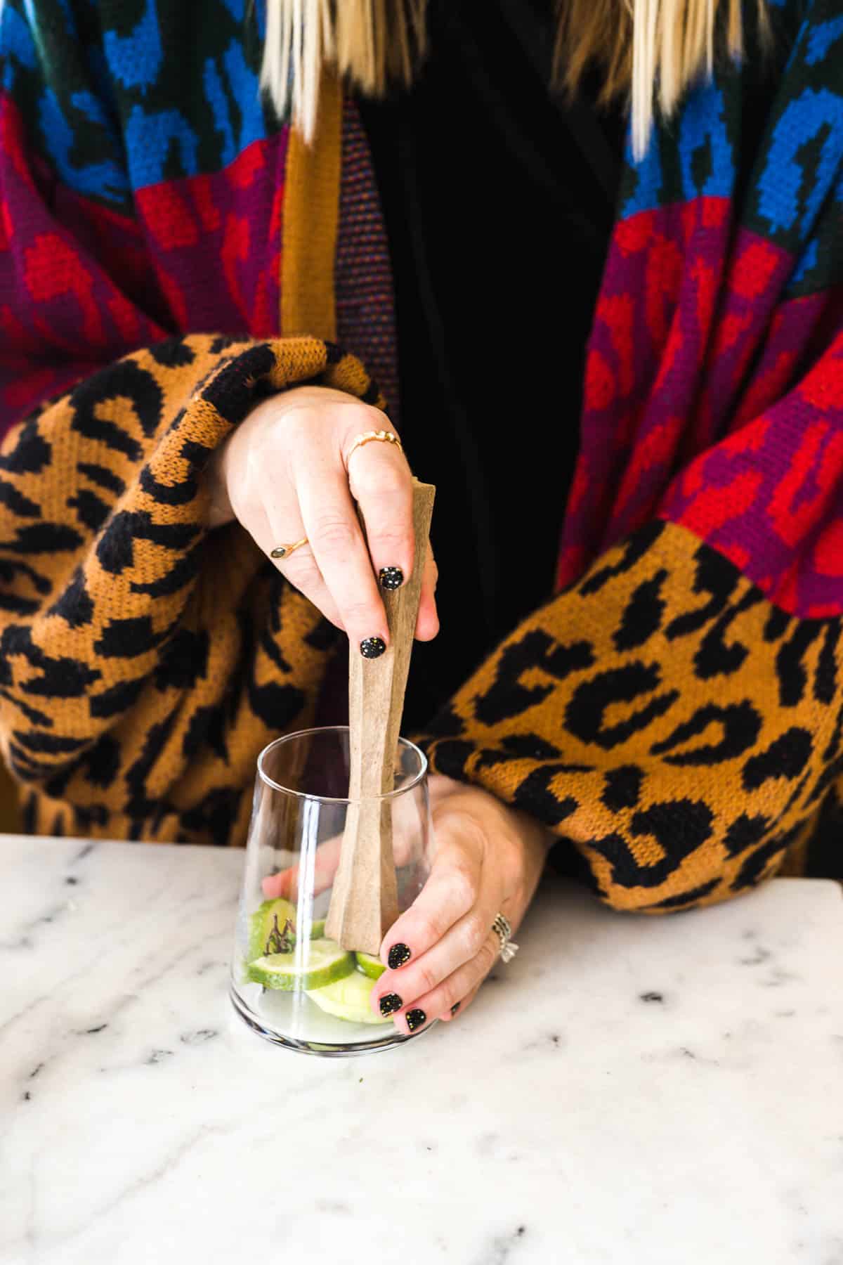 Woman muddling aromatics in the bottom of a cocktail glass.
