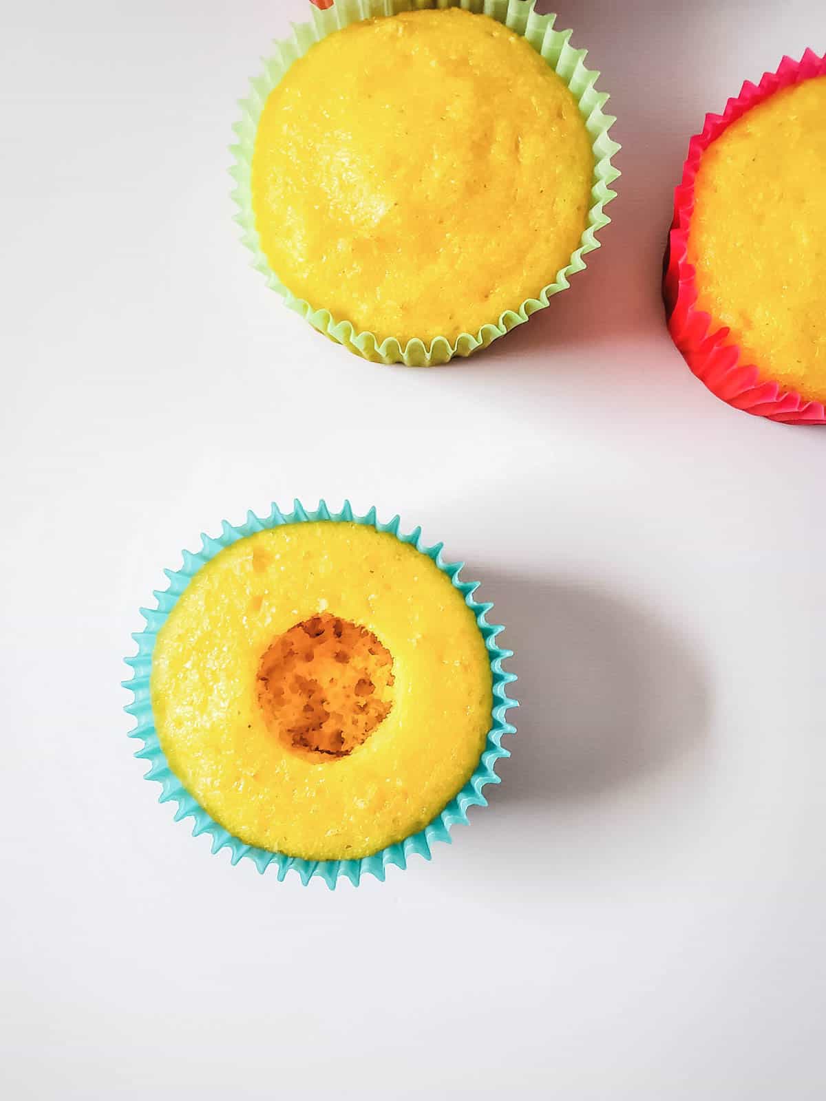 Baked cupcakes on a table with a hole cut out of the center of one of them.