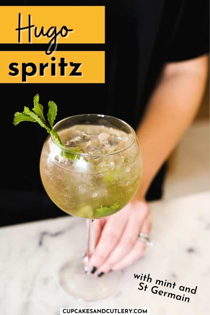 Woman placing a spritz in a balloon glass down on a wooden countertop.