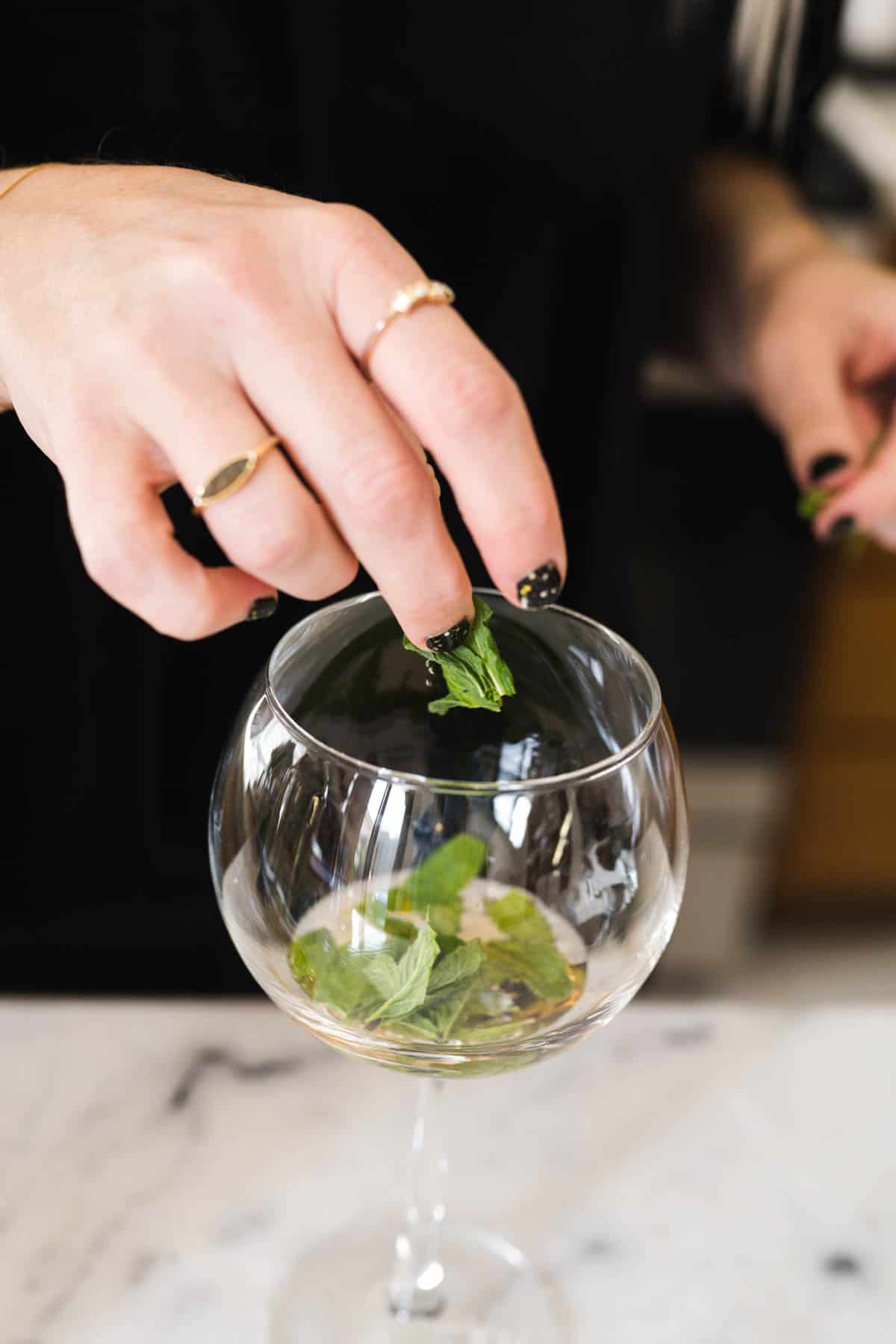 Woman adding mint leaves to a spritz glass of St Germain.