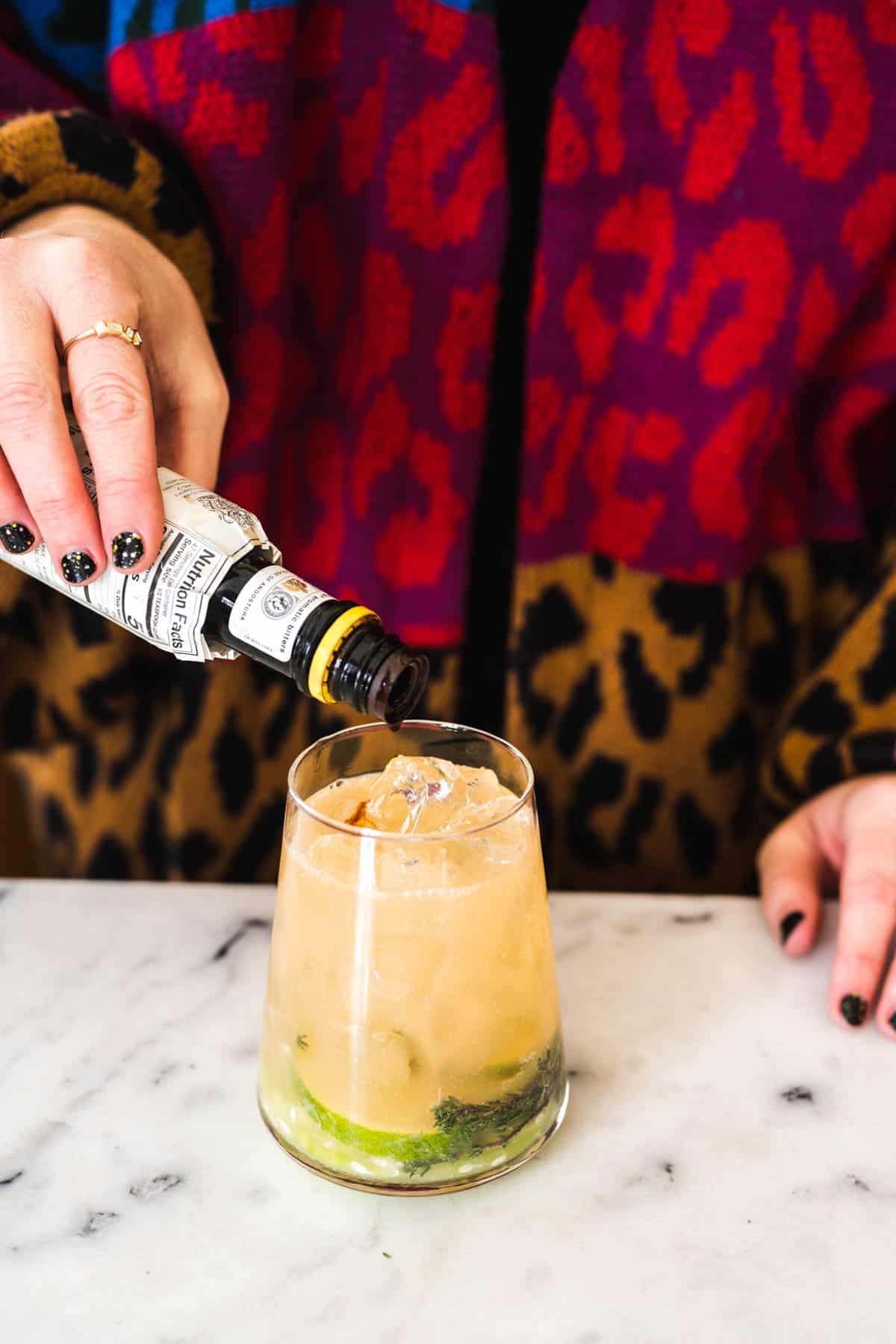 Woman pouring bitters into a grapefruit mocktail.