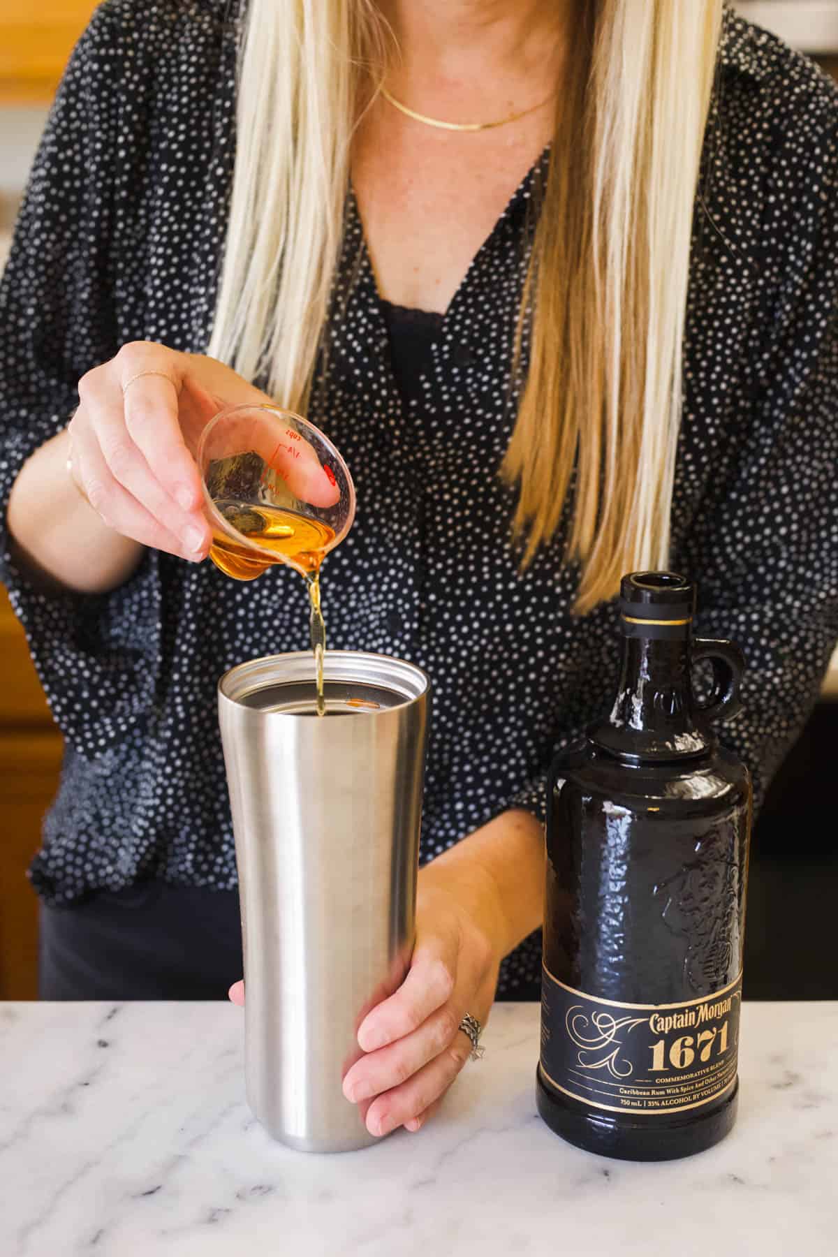 A woman pouring spiced rum into a cocktail shaker.