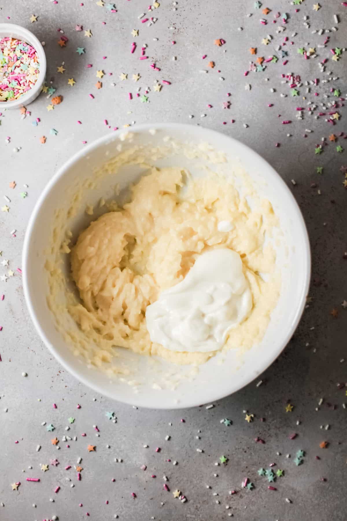 A white mixing bowl filled with ingredients to make buttercream frosting next to a small bowl filled with sprinkles.