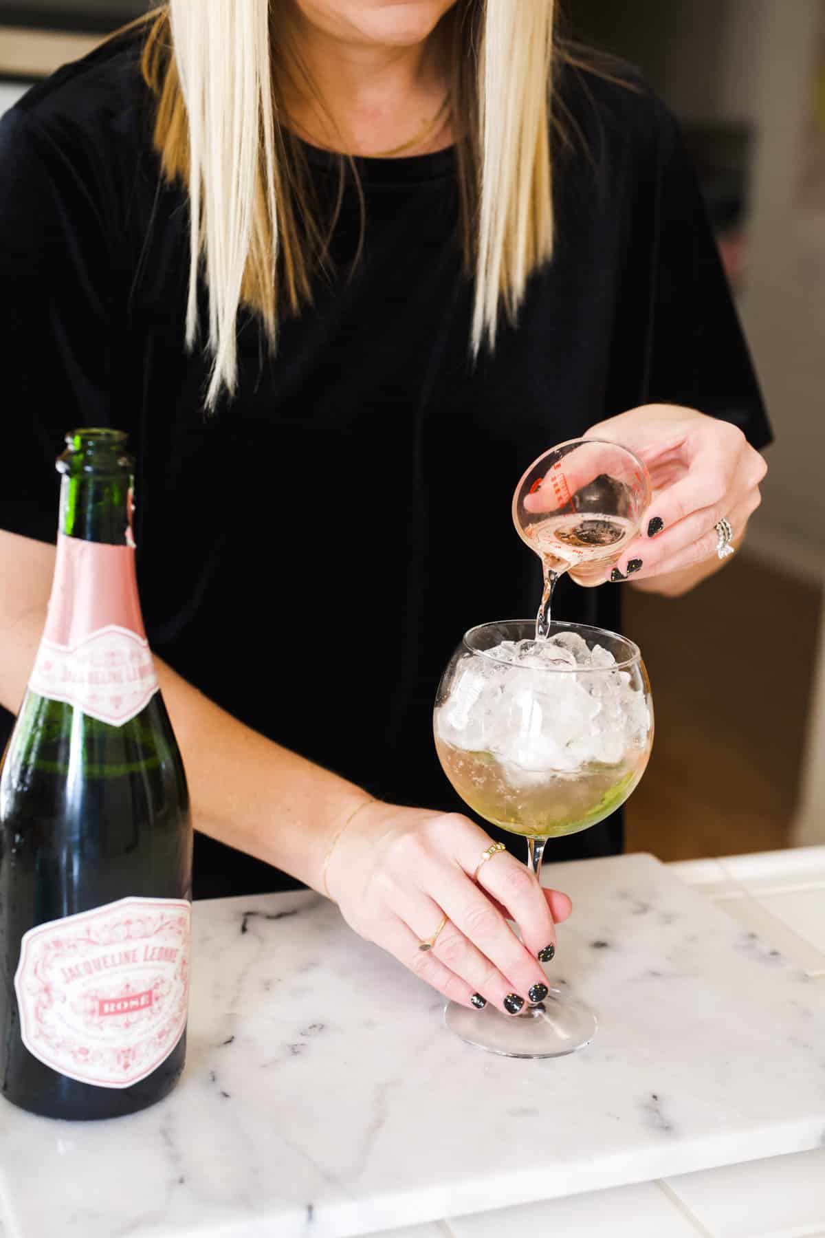 Woman measuring pink Prosecco into a cocktail.