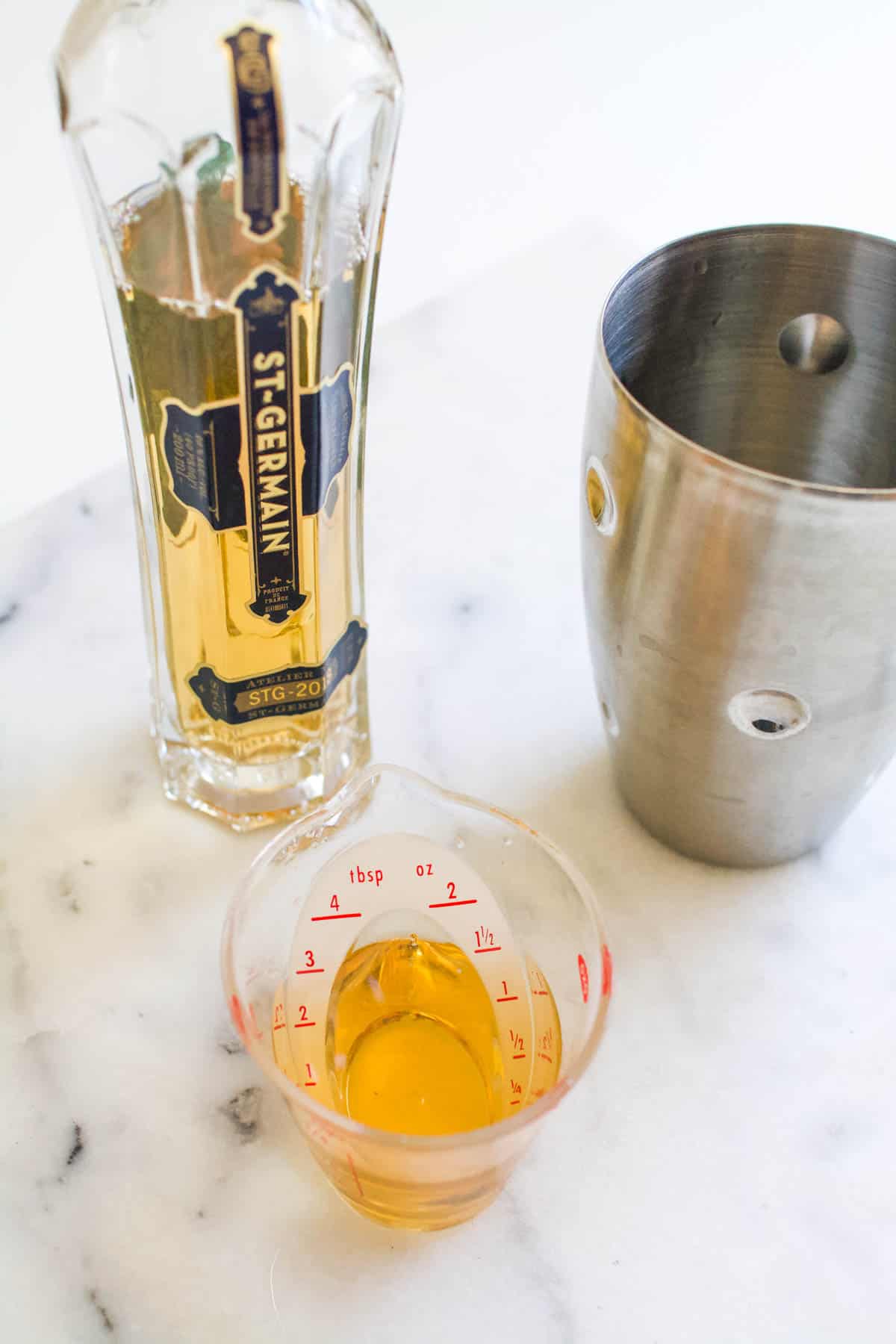 A bottle of St. Germain next to a cocktail shaker and a measuring cup.