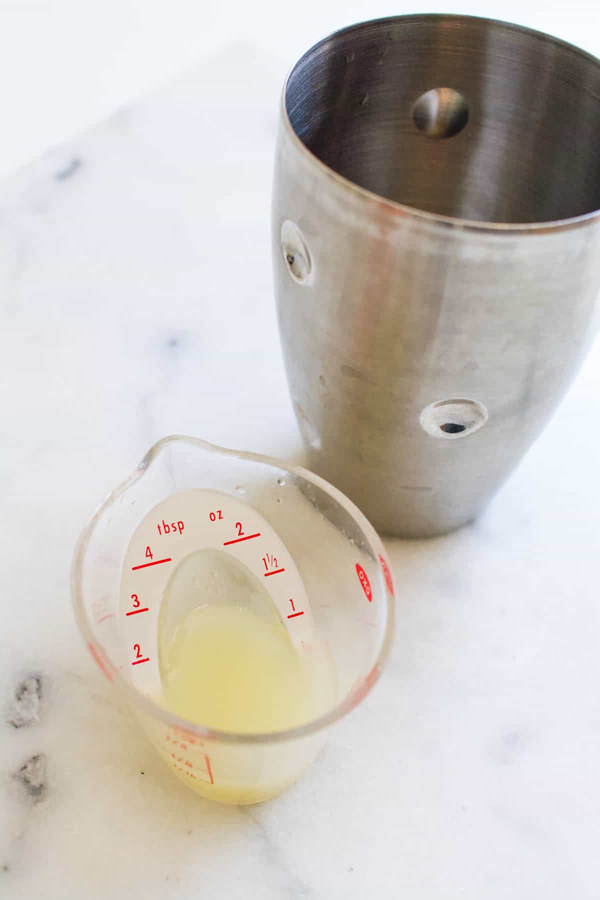 Cocktail shaker next to a liquid measuring cup with lime juice.