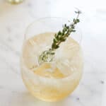 A glass filled with a white wine spritzer made with St. Germain liqueur and topped with a rosemary sprig.