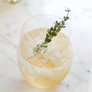 A glass filled with a white wine spritzer made with St. Germain liqueur and topped with a rosemary sprig.