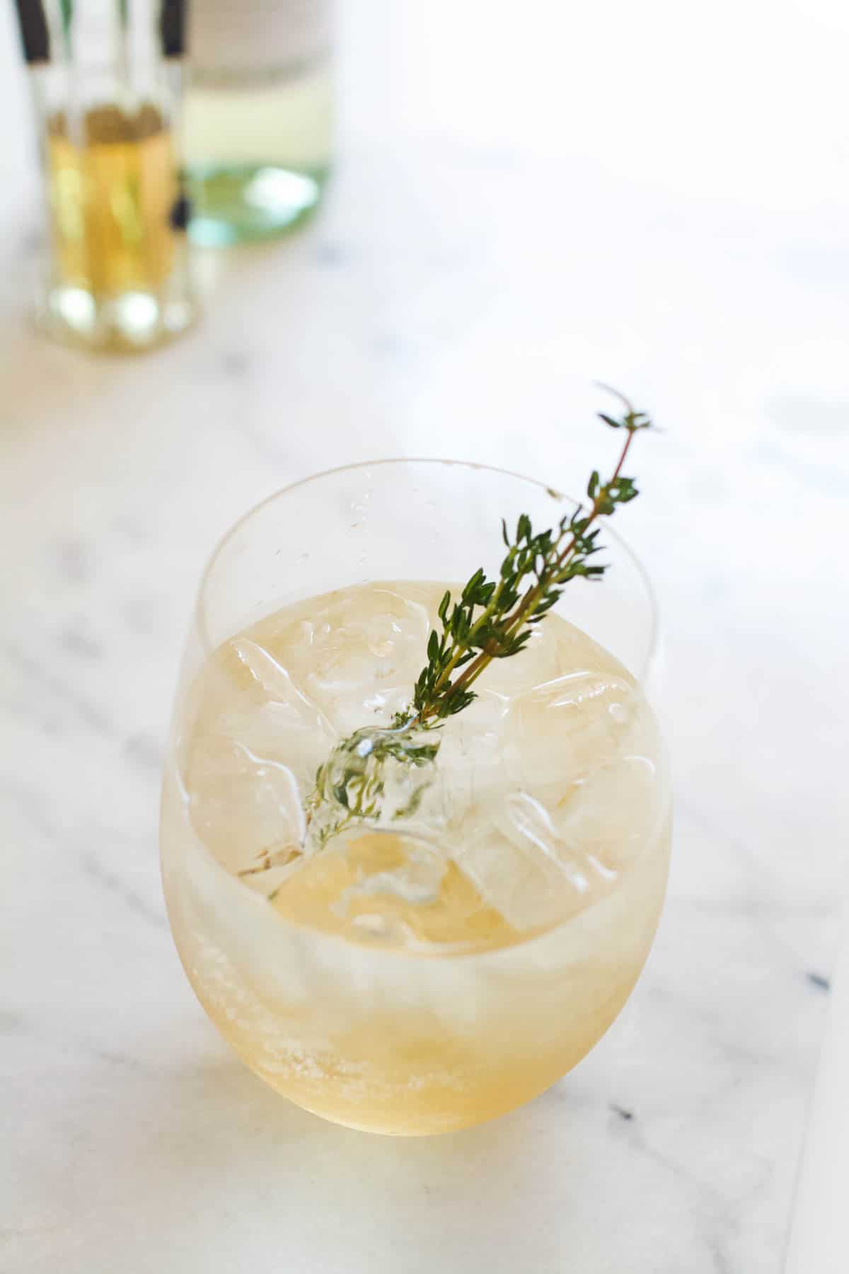 A St. Germain Spritzer in a glass garnished with a sprig of rosemary on a white marble countertop.