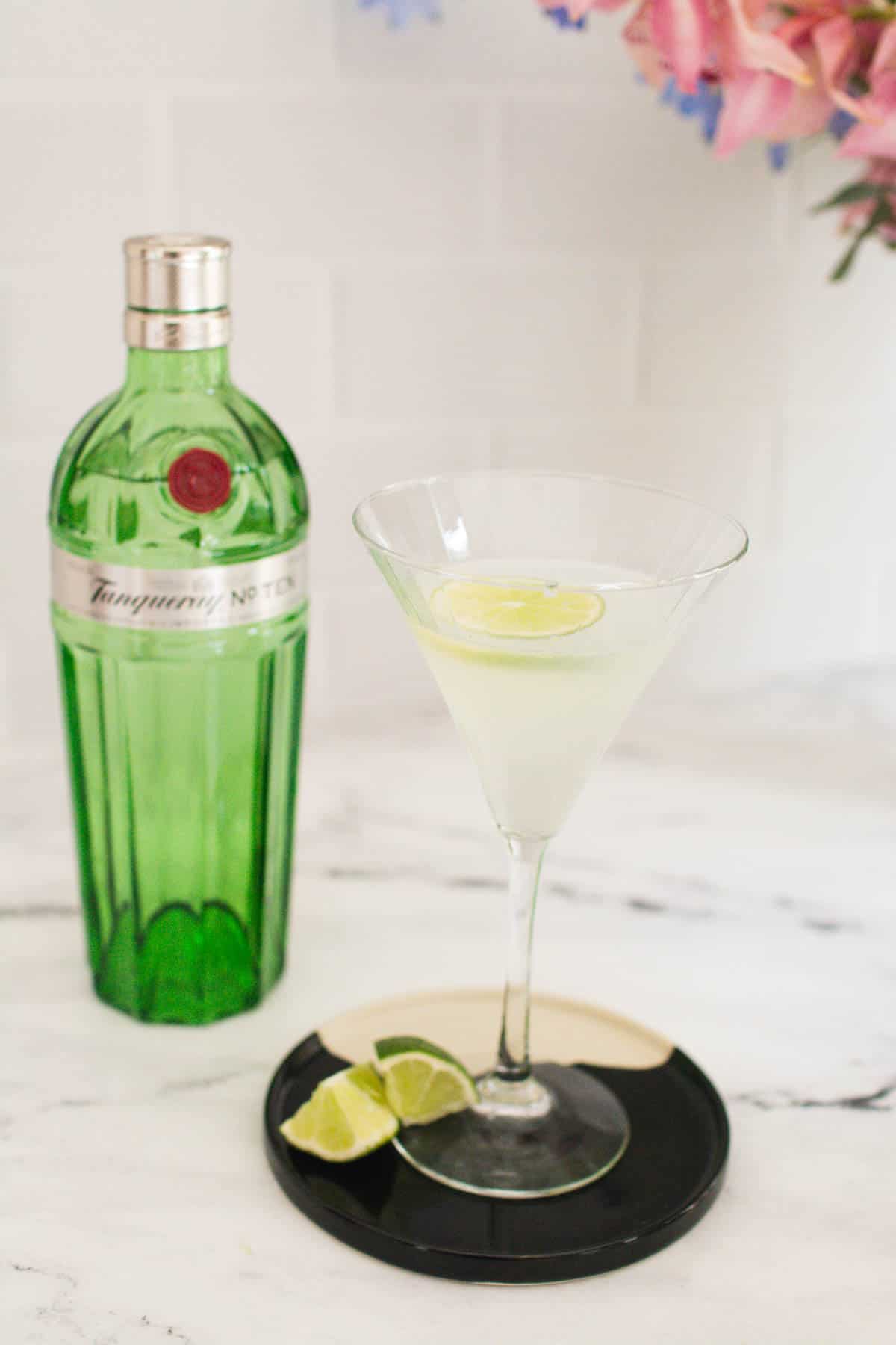 Gimlet in a martini glass next to a bottle of gin.