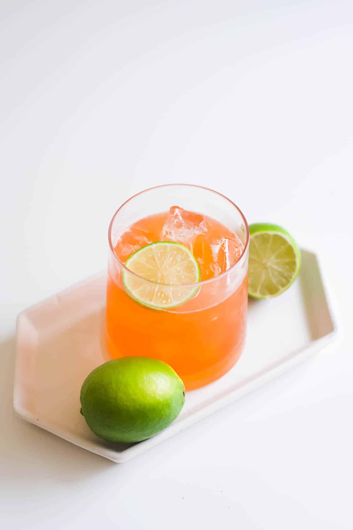 Spiced rum Aperol cocktail in a glass surrounded by limes on top of a small white plate.