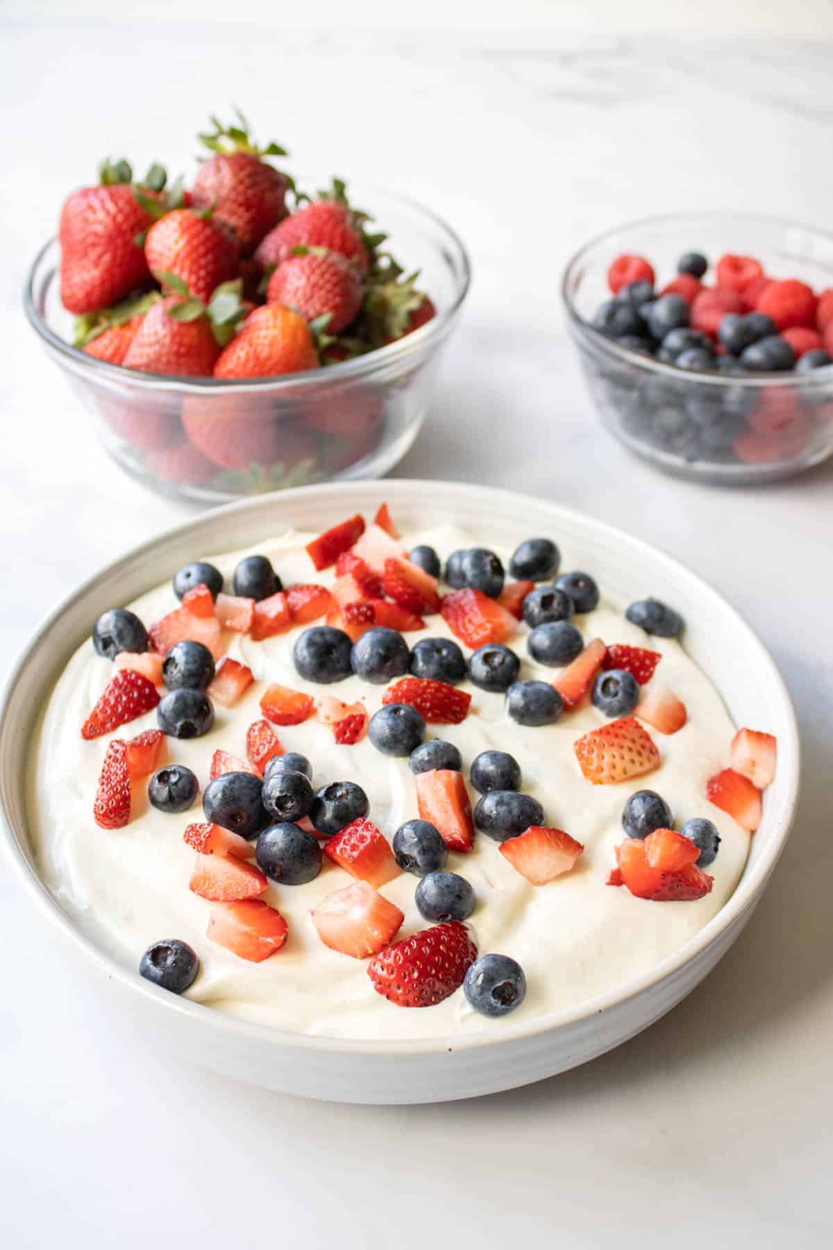 A white bowl on a table with a cheesecake fruit dip topped with red berries for 4th of july.