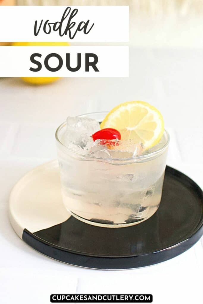 Vodka sour garnished with a cherry and lemon wheel sitting on a white and black tray.