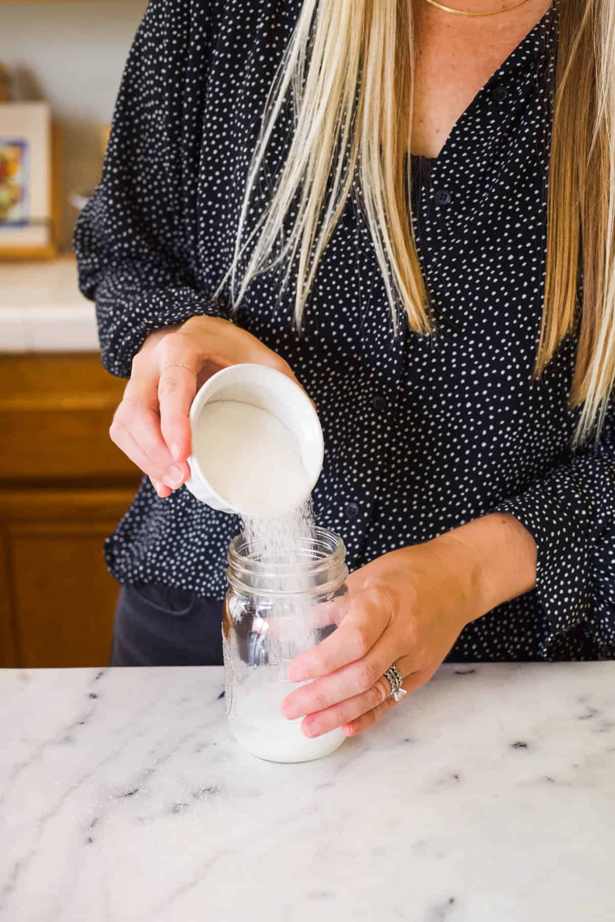 Woman pouring sugar into a mason jar of water.