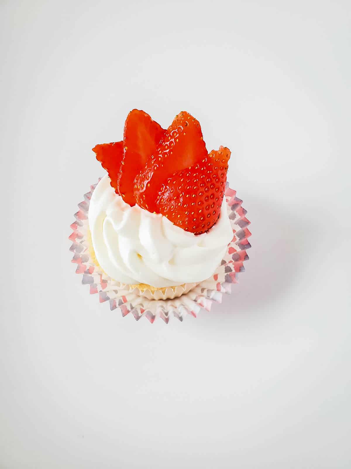 A white frosted cupcake on a table topped with sliced strawberries.