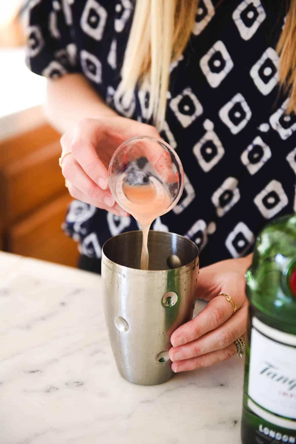 Woman pouring grapefruit juice into a cocktail shaker.