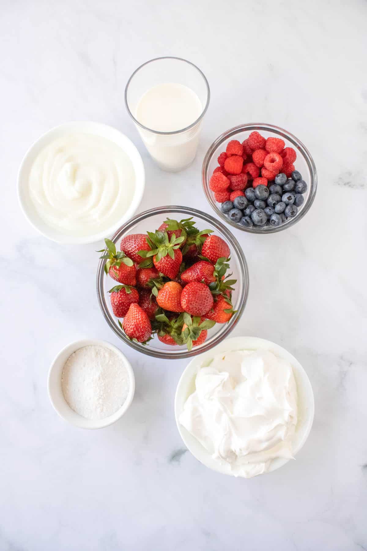 Ingredients to make cheesecake dip in small bowls with bowls of fresh berries.